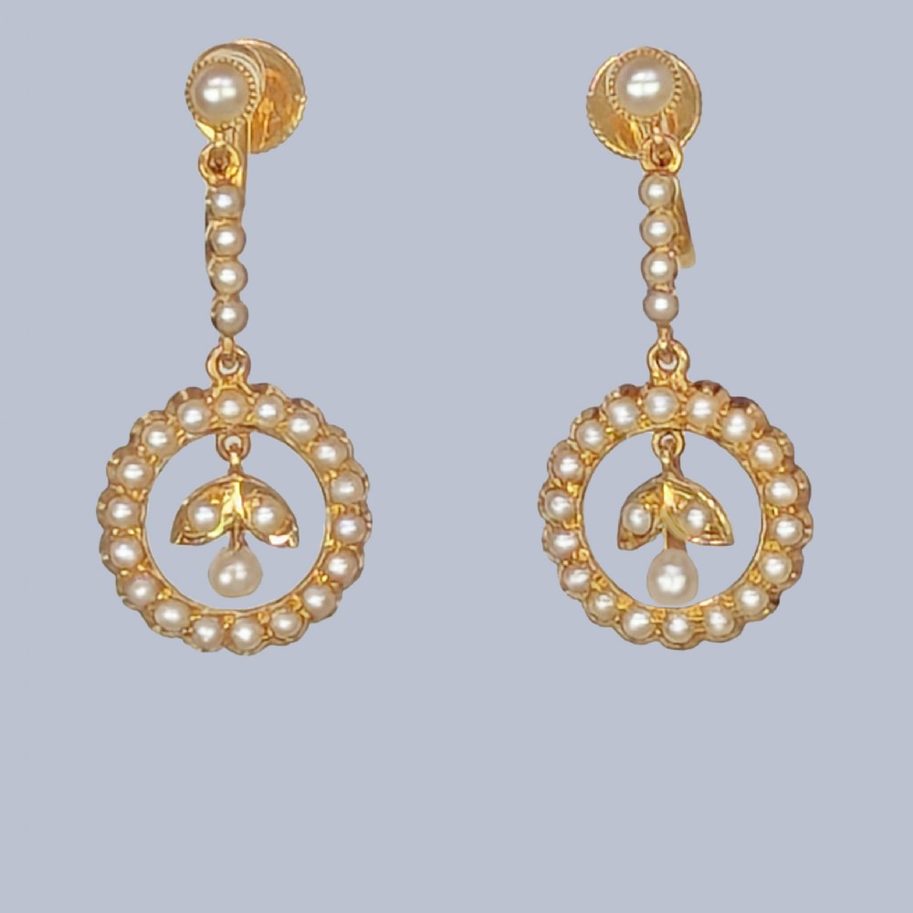 A pair of Edwardian 15ct yellow gold drop earrings featuring circular seed pearl frames around foliate central motifs with screw-back fittings.