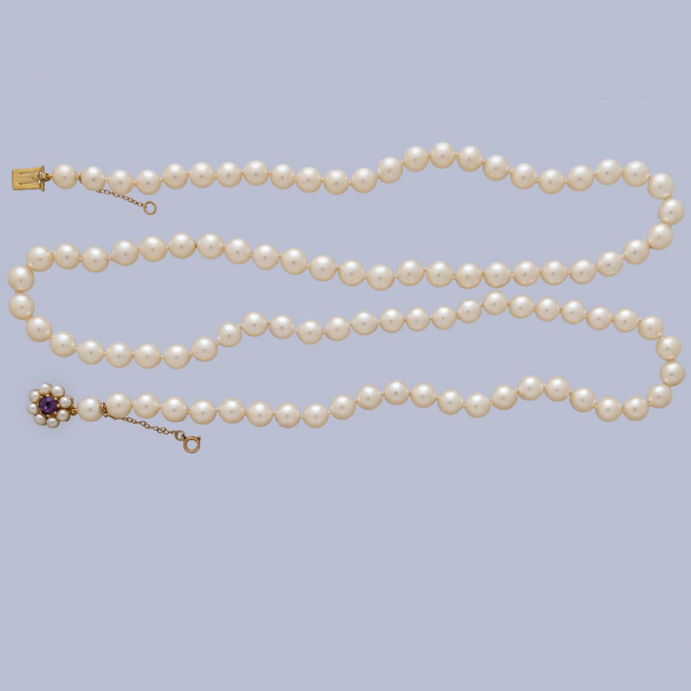 A long single strand of creamy white cultured pearls featuring a 9ct gold flower cluster clasp set with a central purple amethyst.