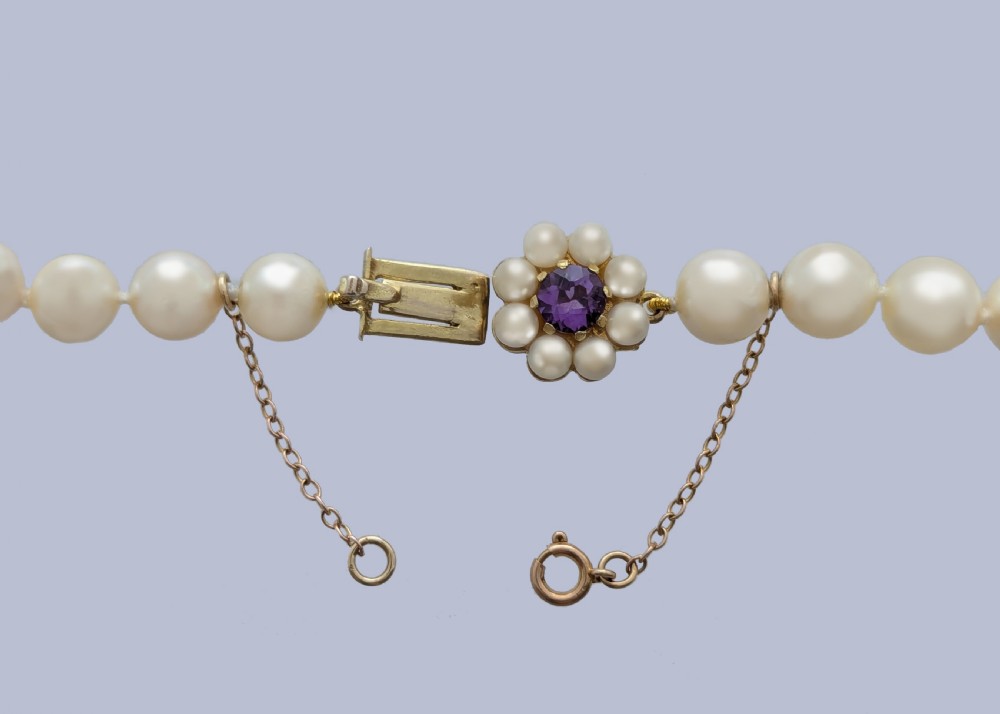 A long single strand of creamy white cultured pearls featuring a 9ct gold flower cluster clasp set with a central purple amethyst. View V