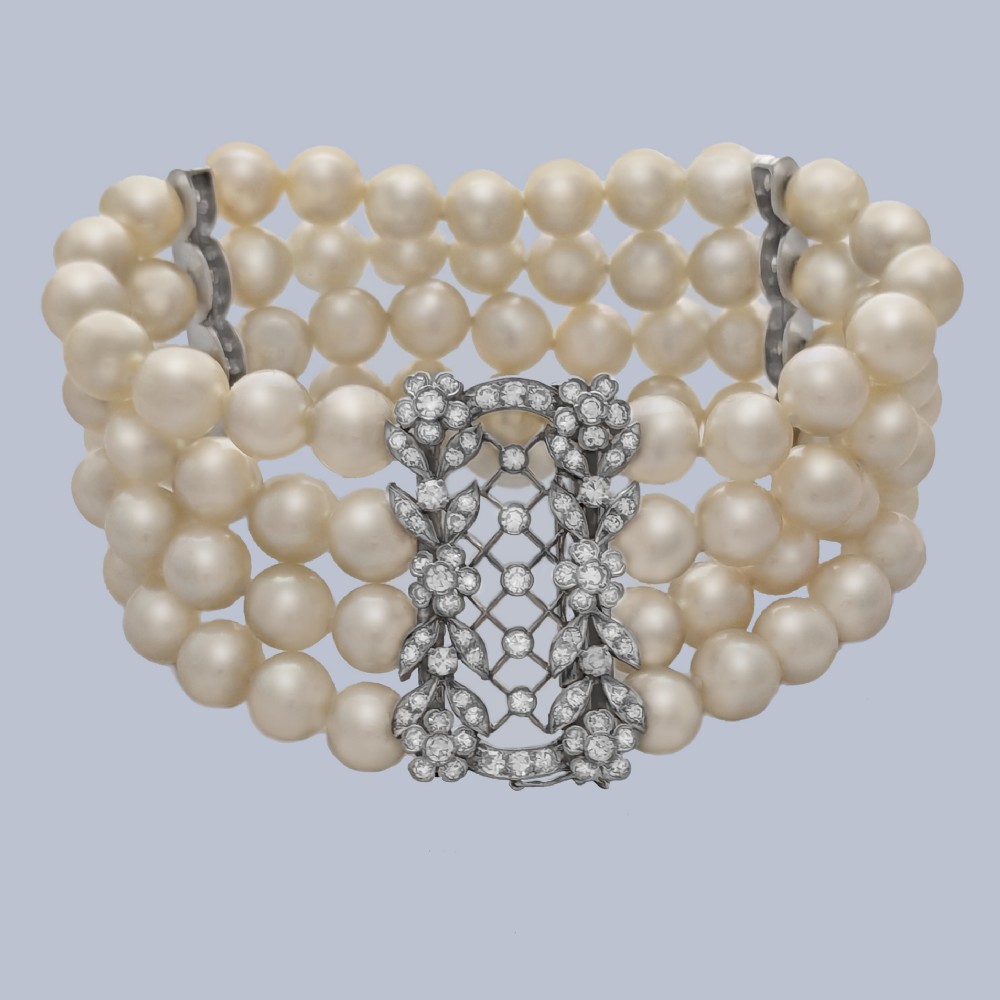 An Edwardian four-strand pearl bracelet featuring a central openwork diamond floral clasp in white metal.