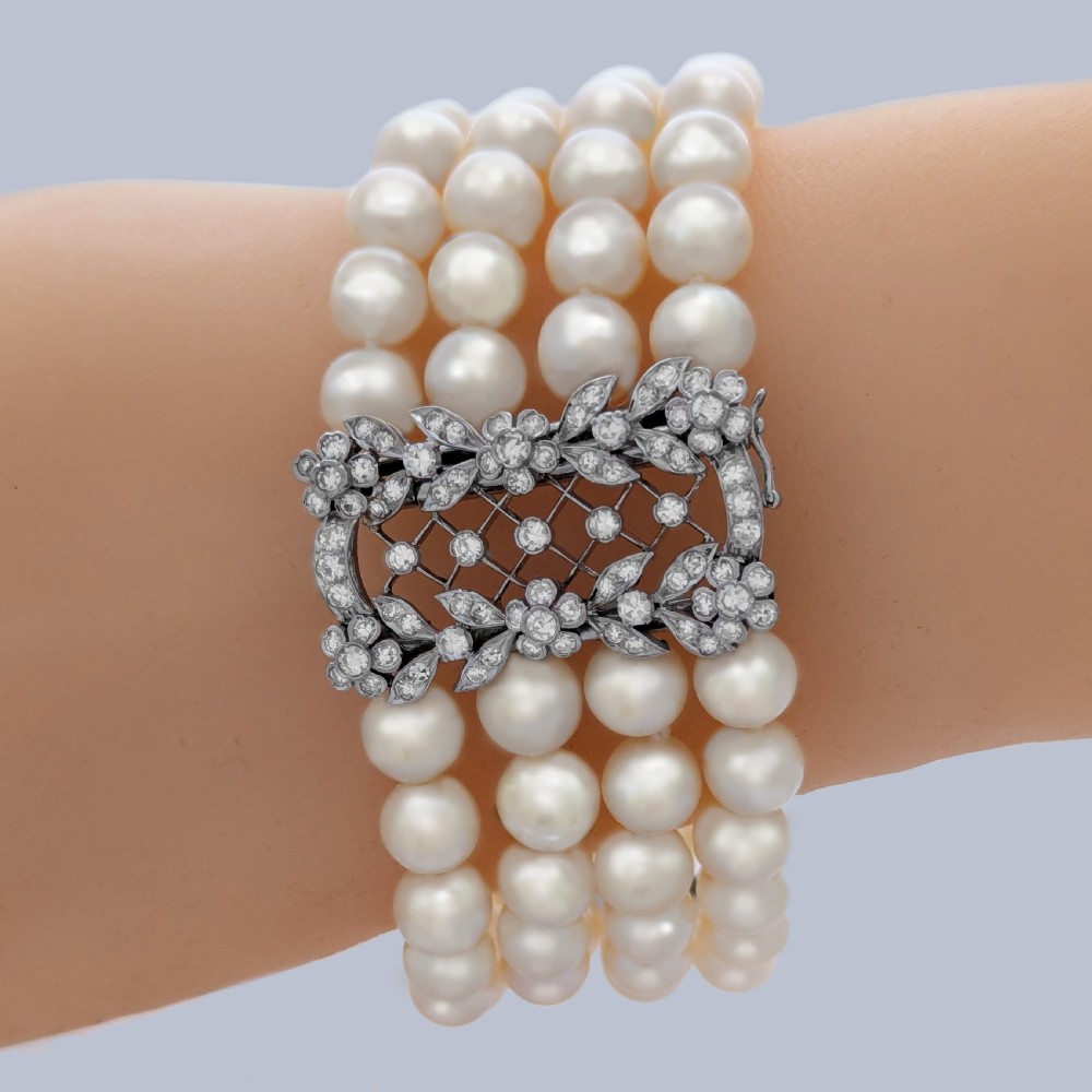 An Edwardian four-strand pearl bracelet featuring a central openwork diamond floral clasp in white metal. View II