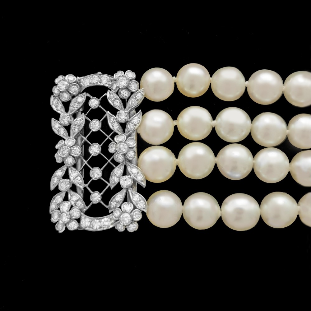 An Edwardian four-strand pearl bracelet featuring a central openwork diamond floral clasp in white metal. View VIII