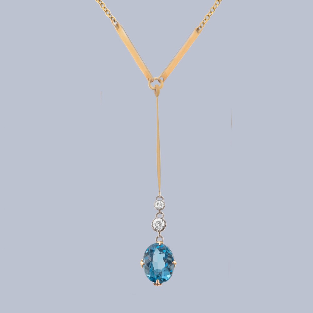 An Edwardian 15ct yellow gold lavalier pendant necklace featuring a geometric bar drop, two millegrain-set old cut diamonds, and an oval blue topaz gemstone.