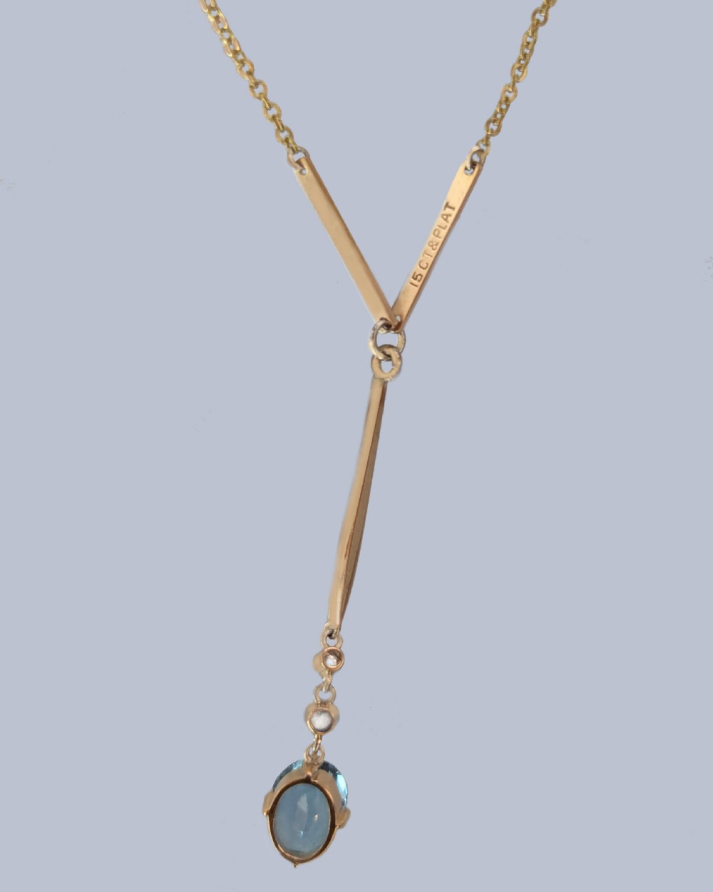 An Edwardian 15ct yellow gold lavalier pendant necklace featuring a geometric bar drop, two millegrain-set old cut diamonds, and an oval blue topaz gemstone. View V