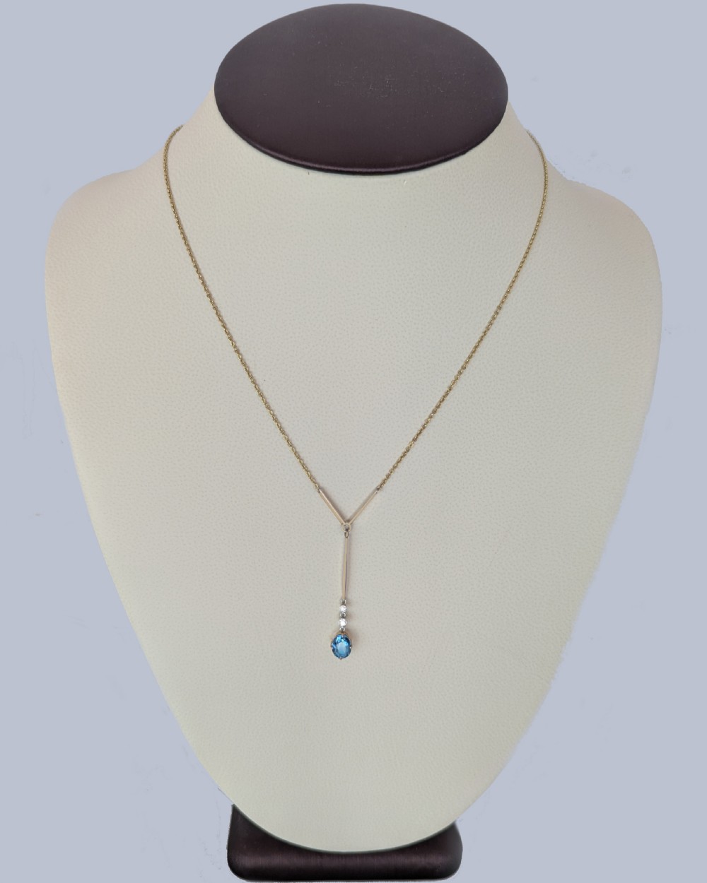 An Edwardian 15ct yellow gold lavalier pendant necklace featuring a geometric bar drop, two millegrain-set old cut diamonds, and an oval blue topaz gemstone. View VII