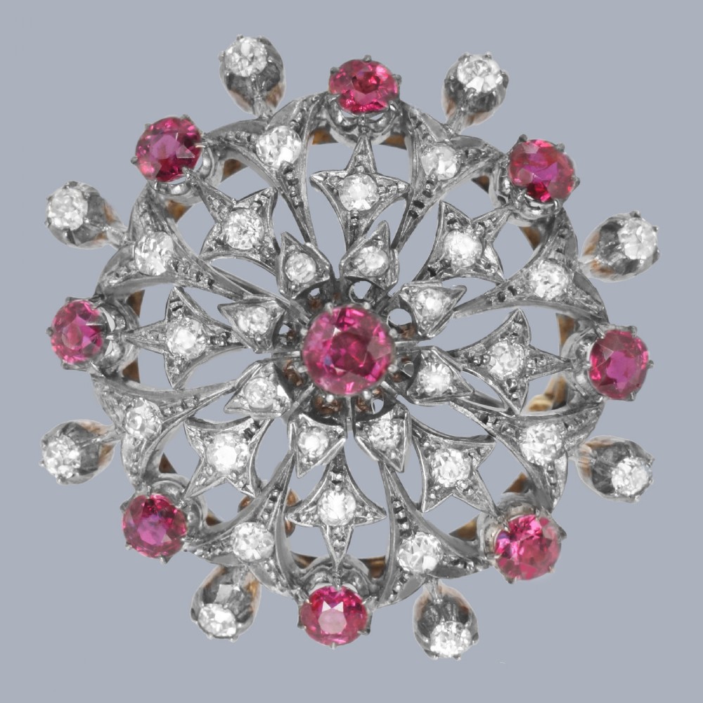 A circular Victorian brooch rendered in silver and gold, featuring a central round ruby surrounded by intricate diamond-set starburst openwork and an outer border of alternating rubies and diamonds.