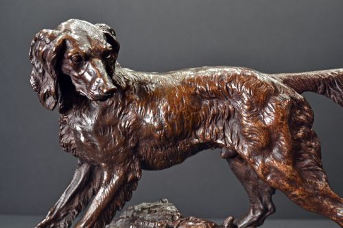 fig 1. A dark brown patinated bronze sculpture depicting a setter dog standing over a rabbit on a textured ground base.