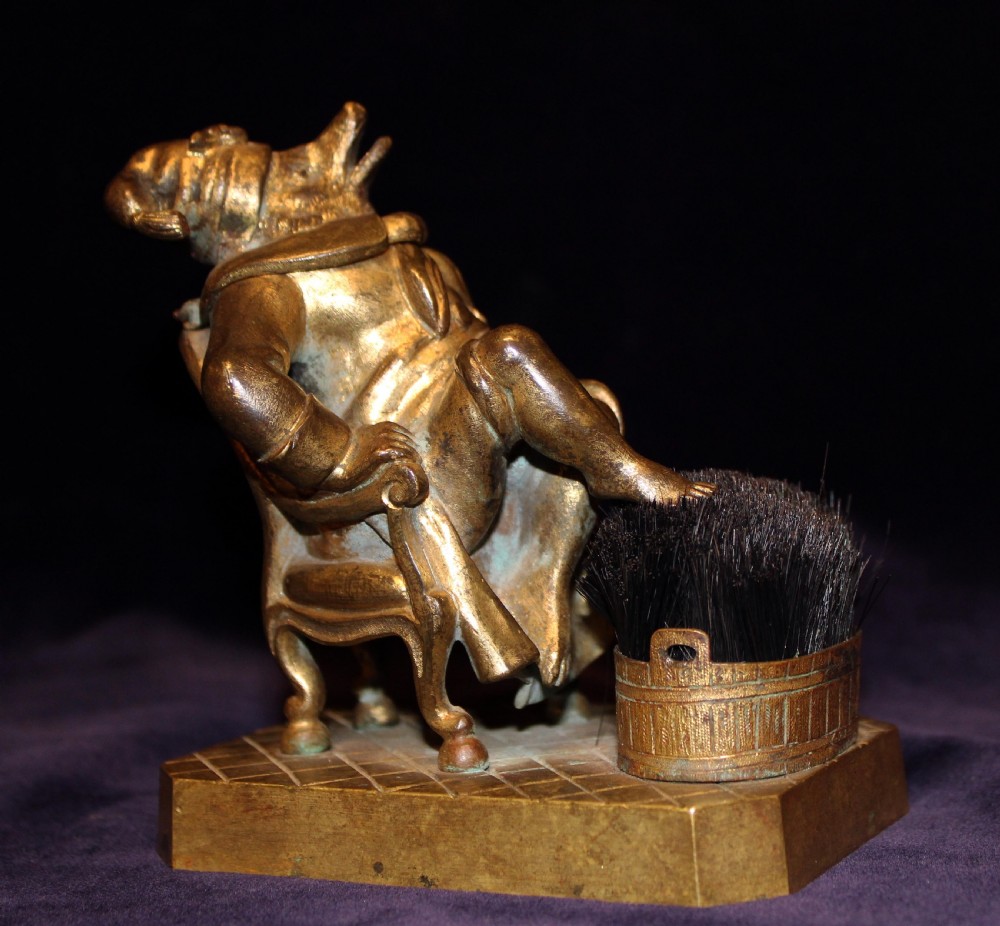 An antique gilt bronze desk accessory depicting an anthropomorphic fox wearing a nightgown and nightcap seated in an armchair with his foot resting on a bristle pen wiper.