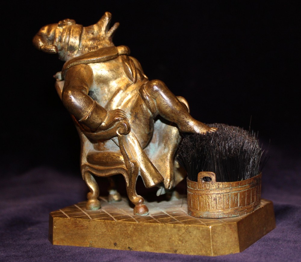 An antique gilt bronze desk accessory depicting an anthropomorphic fox wearing a nightgown and nightcap seated in an armchair with his foot resting on a bristle pen wiper. View II