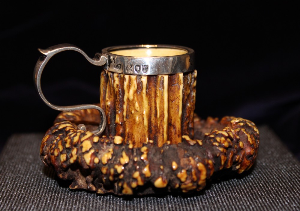 An antique chamberstick crafted from textured brown deer antler with a fitted silver rim and loop handle.