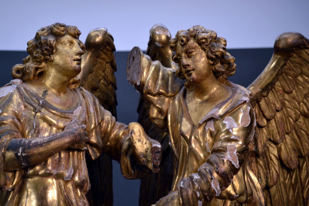 Two antique carved wooden figures of archangels with large wings, finished in distressed gold leaf and standing on a red-painted rectangular base. View II