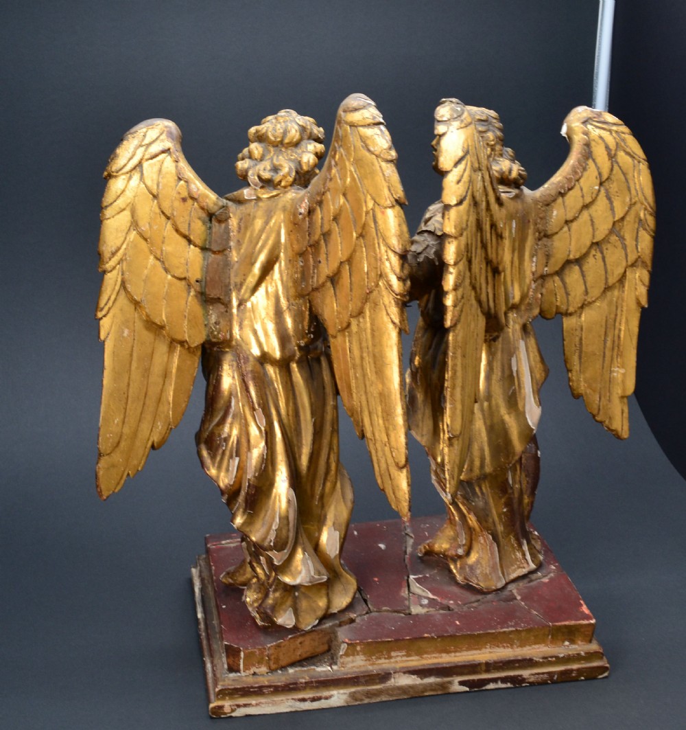 Two antique carved wooden figures of archangels with large wings, finished in distressed gold leaf and standing on a red-painted rectangular base. View III