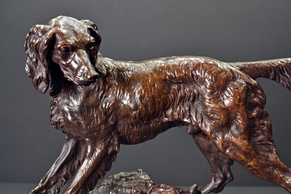 A dark brown patinated bronze sculpture depicting a setter dog standing over a rabbit on a textured ground base. View II