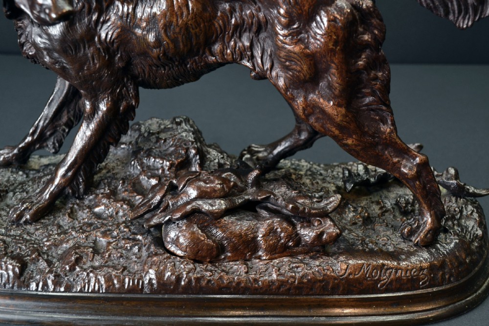 A dark brown patinated bronze sculpture depicting a setter dog standing over a rabbit on a textured ground base. View III