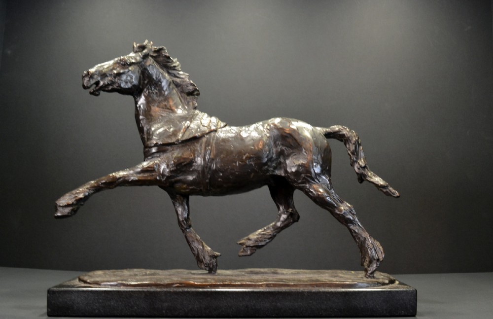 A dark bronze sculpture of a trotting cob horse mounted on a rectangular black stone base.