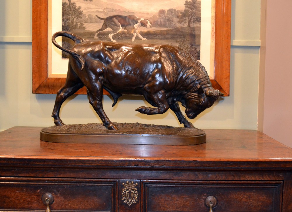A dark patinated bronze sculpture depicting a muscular charging bull on an integral oval bronze base. View II