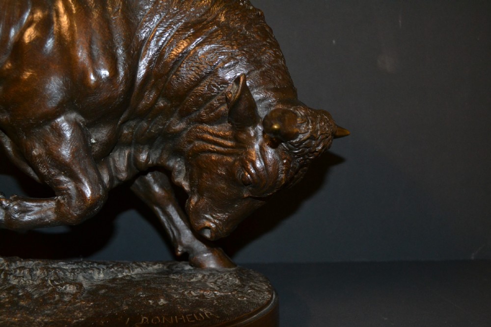 A dark patinated bronze sculpture depicting a muscular charging bull on an integral oval bronze base. View III