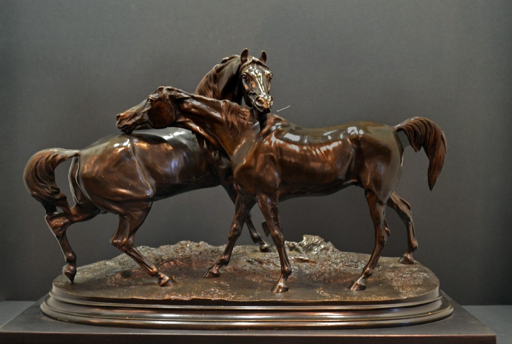A dark brown bronze equestrian sculpture depicting an Arabian stallion and mare interacting on an oval naturalistic base.