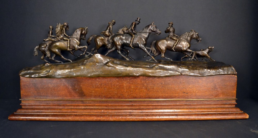 A detailed dark bronze sculpture depicting multiple riders on horseback following hunting hounds, mounted on a rectangular wooden base. View II