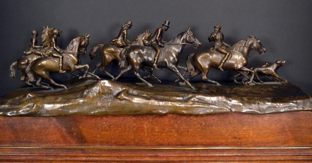 A detailed dark bronze sculpture depicting multiple riders on horseback following hunting hounds, mounted on a rectangular wooden base. View IV