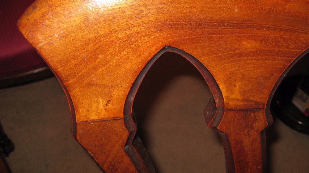 A Victorian mahogany dining chair featuring carved Gothic arched back splats, a crimson upholstered seat, and turned front legs on brass castors. View II
