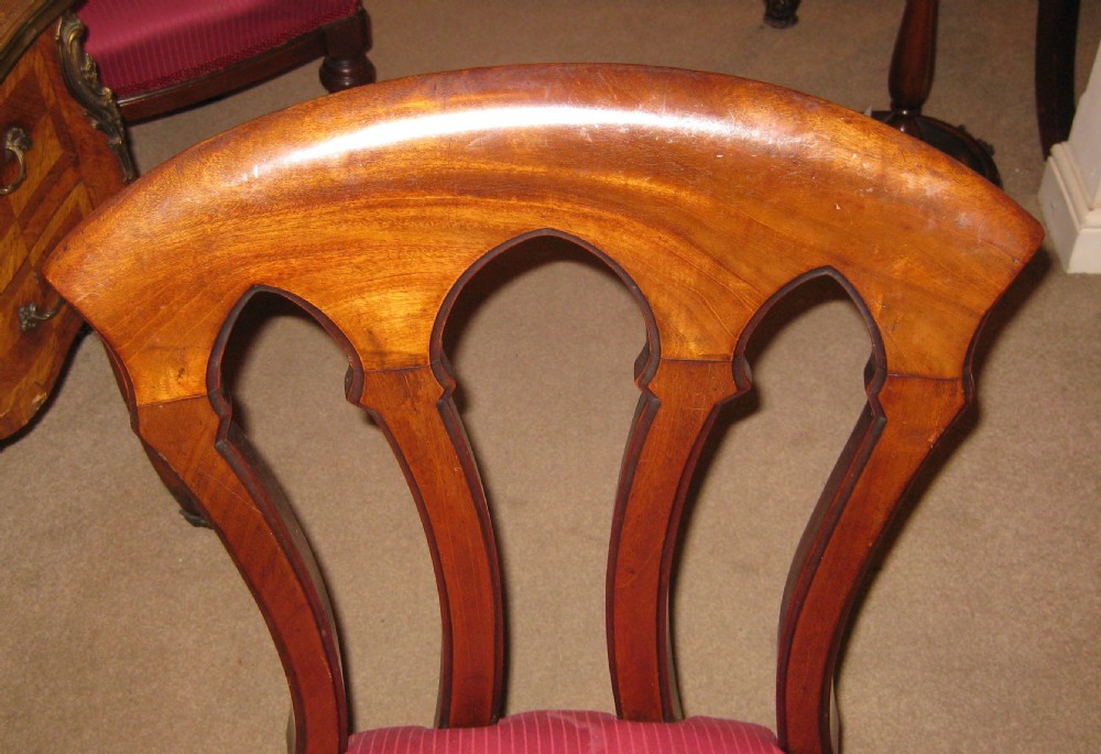 A Victorian mahogany dining chair featuring carved Gothic arched back splats, a crimson upholstered seat, and turned front legs on brass castors. View III