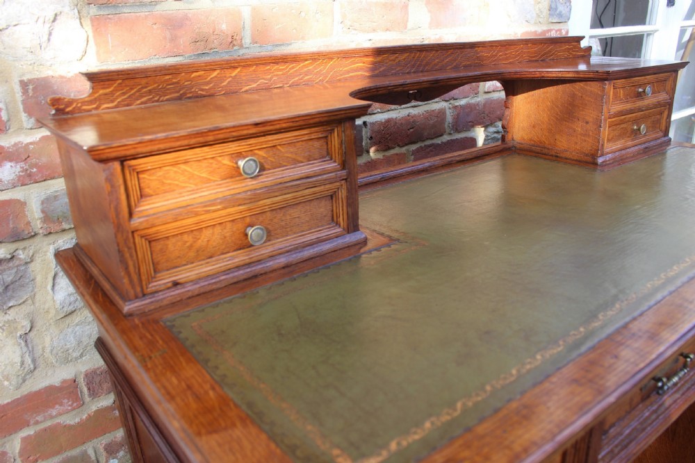 A Victorian golden oak pedestal desk featuring a green leather writing insert, twin pedestals of drawers, brass handles, and a raised top gallery. View III