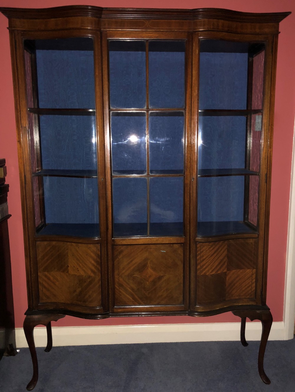A late Victorian mahogany glazed display cabinet featuring three central glass doors above geometric inlaid timber panels, resting on cabriole legs with a blue fabric-lined interior.