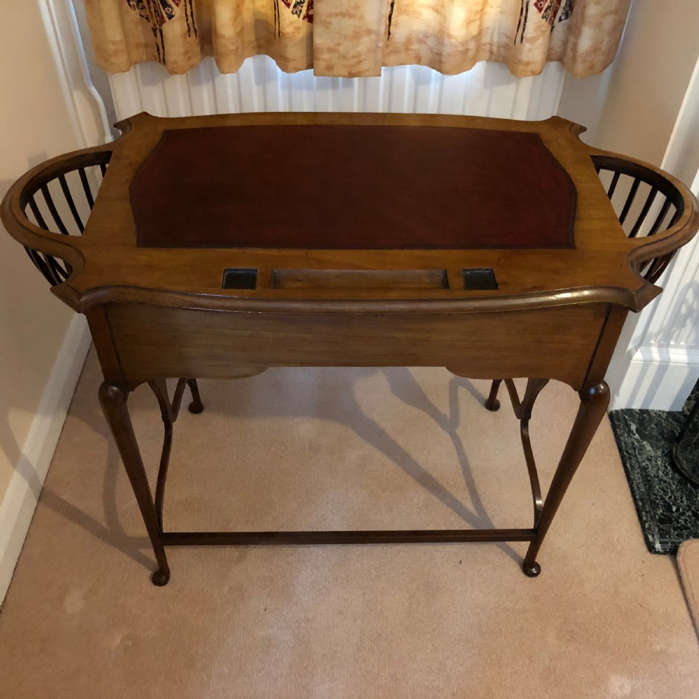 A late Victorian mahogany writing table featuring a shaped red leather inset writing surface, integrated inkwell compartments, and spindle-turned side galleries supported by slender cabriole legs.