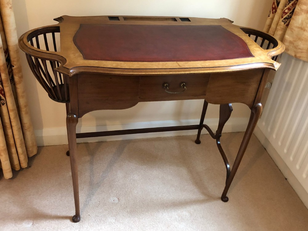 A late Victorian mahogany writing table featuring a shaped red leather inset writing surface, integrated inkwell compartments, and spindle-turned side galleries supported by slender cabriole legs. View V