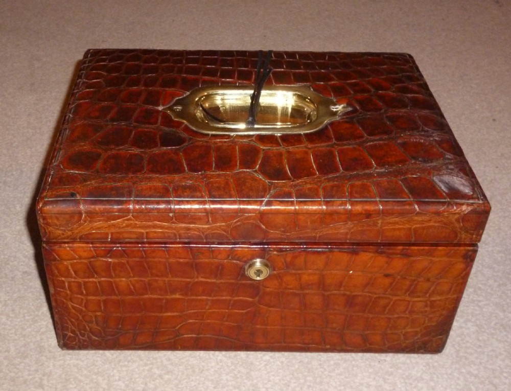 A rectangular warm brown crocodile leather jewellery case featuring a flush recessed brass handle on top and a brass lock keyhole on the front.