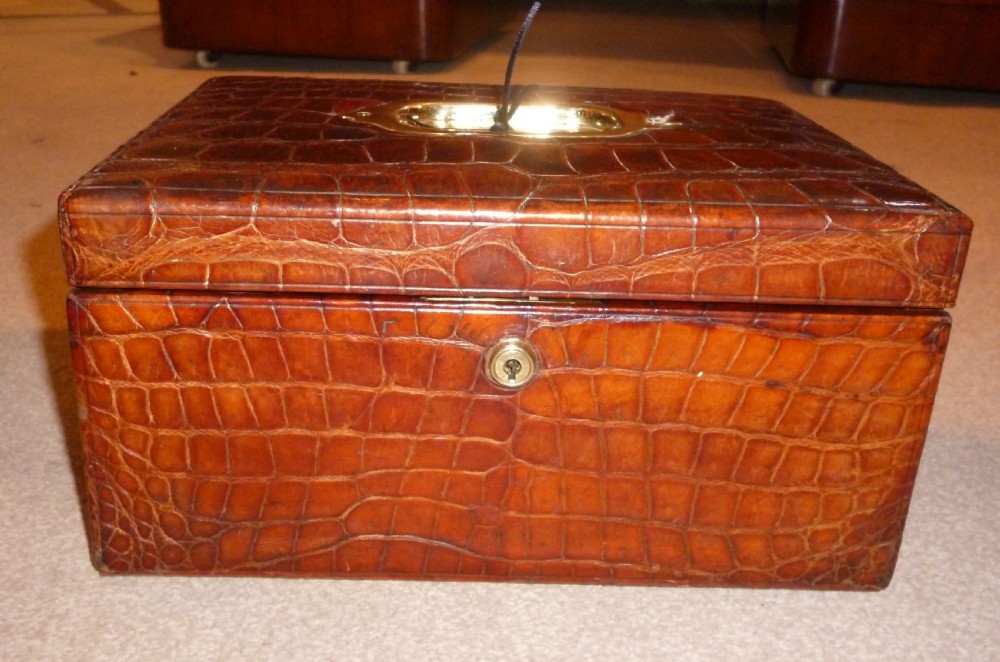 A rectangular warm brown crocodile leather jewellery case featuring a flush recessed brass handle on top and a brass lock keyhole on the front. View II