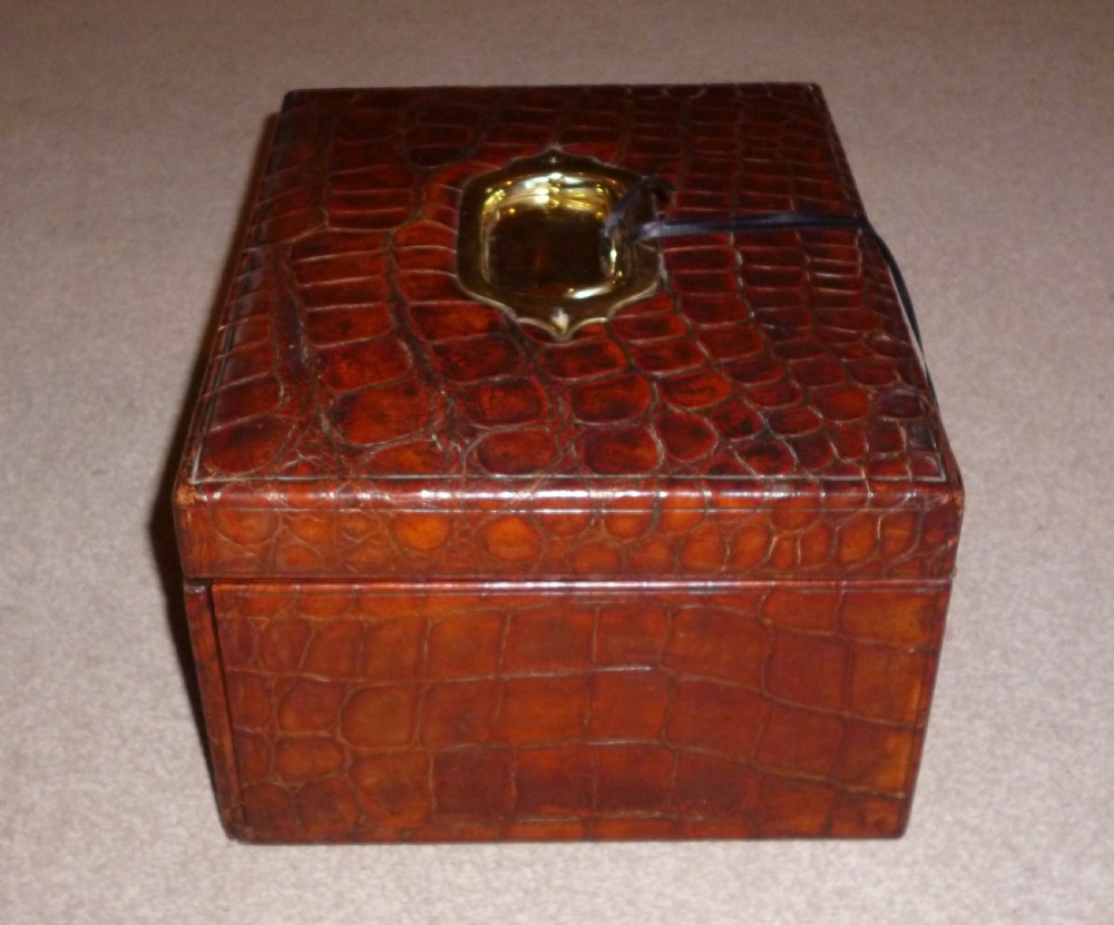 A rectangular warm brown crocodile leather jewellery case featuring a flush recessed brass handle on top and a brass lock keyhole on the front. View V