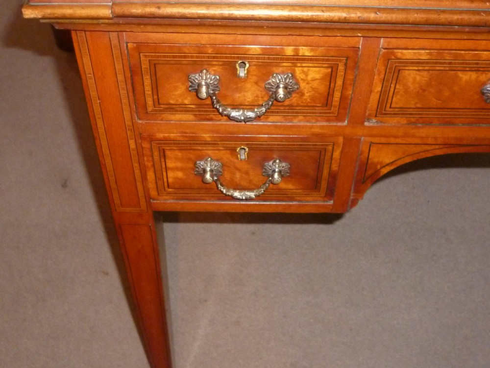 An Edwardian satinwood rolltop bureau featuring a cylinder front with an oval marquetry panel, a brass gallery rail top, and tapered legs. View VI
