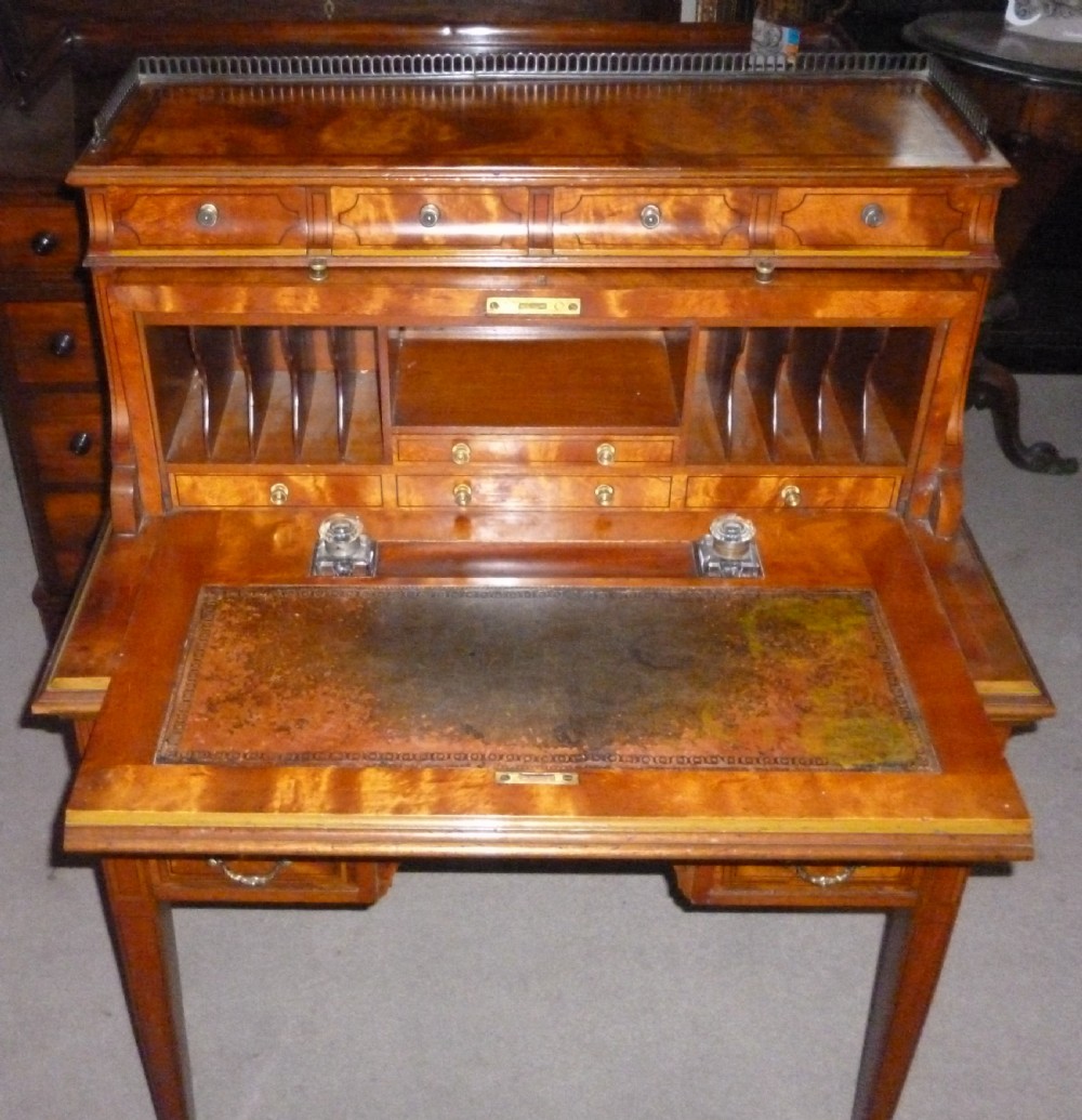 An Edwardian satinwood rolltop bureau featuring a cylinder front with an oval marquetry panel, a brass gallery rail top, and tapered legs. View IX