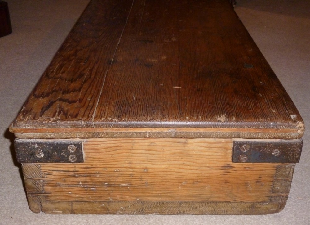 A low rectangular solid pine ammunition box featuring dark metal corner brackets and a central front latch. View III