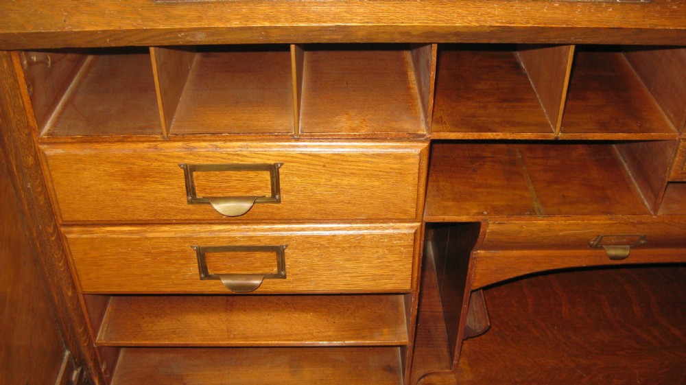 An Edwardian solid oak roll-top desk featuring an S-curved tambour front, twin pedestals with drawers, and carved wooden handles. View VI