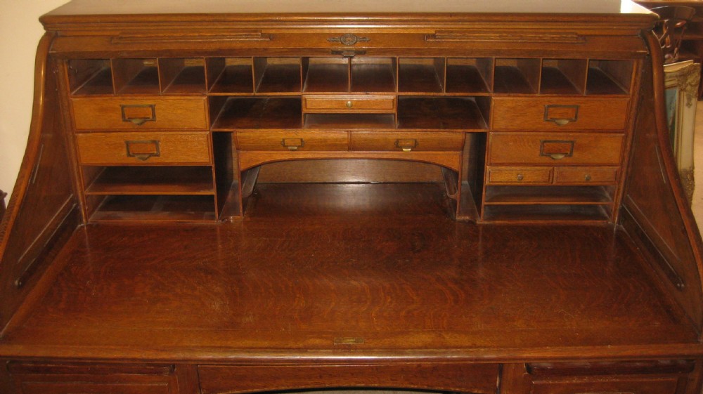An Edwardian solid oak roll-top desk featuring an S-curved tambour front, twin pedestals with drawers, and carved wooden handles. View IX