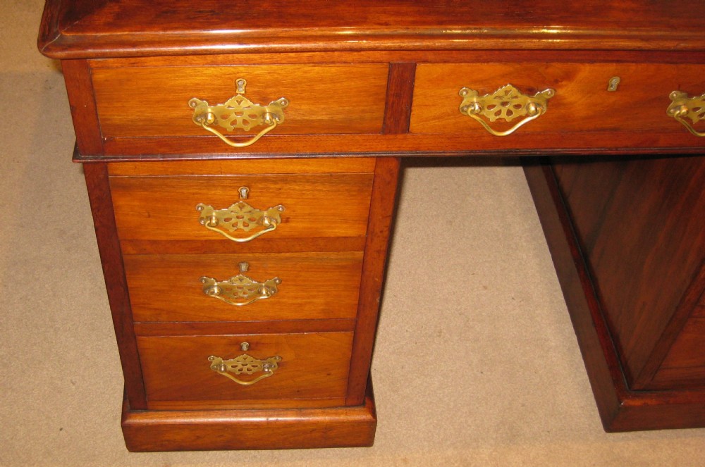 A Victorian walnut pedestal desk featuring nine drawers with decorative brass handles and a dark leather inset writing top. View VI