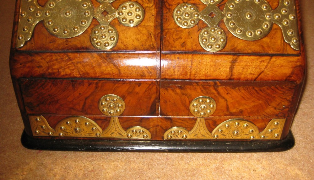 A Victorian burr walnut stationery cabinet featuring a sloped front adorned with ornate, studded brass strapwork mounts. View VII