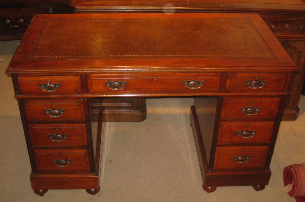 A late Victorian golden walnut pedestal desk featuring a leather-inset writing surface, nine drawers with brass handles, and turned feet.