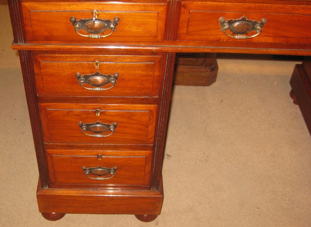 A late Victorian golden walnut pedestal desk featuring a leather-inset writing surface, nine drawers with brass handles, and turned feet. View II