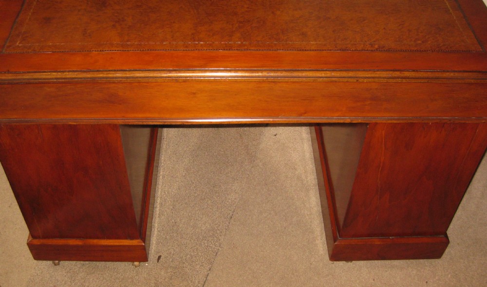 A late Victorian golden walnut pedestal desk featuring a leather-inset writing surface, nine drawers with brass handles, and turned feet. View V