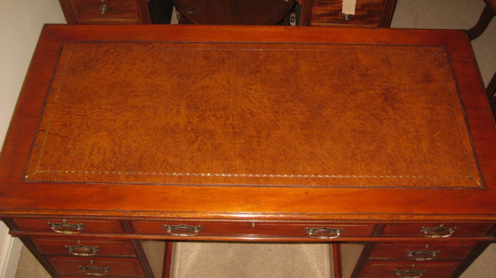 A late Victorian golden walnut pedestal desk featuring a leather-inset writing surface, nine drawers with brass handles, and turned feet. View VII