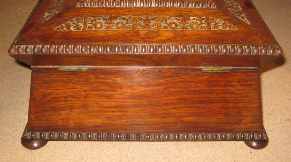 An antique sarcophagus-shaped rosewood sewing box featuring floral brass and mother-of-pearl inlays, carved gadrooned borders, and bun feet. View X