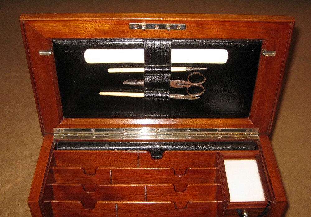 An open antique walnut stationery cabinet featuring a fold-down leather writing slope, internal letter compartments, small drawers, and calendar inserts. View V
