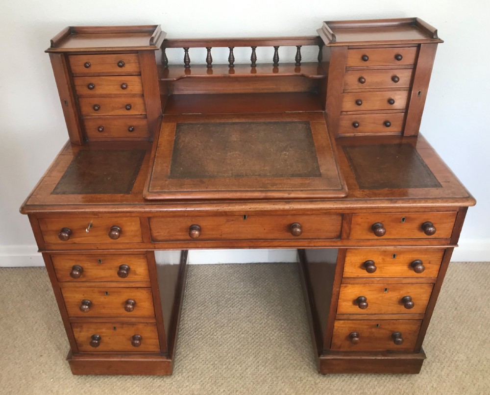 A Victorian golden walnut Dickens desk featuring a central sloped leather writing surface flanked by raised side drawers and a spindle gallery above twin drawer pedestals.