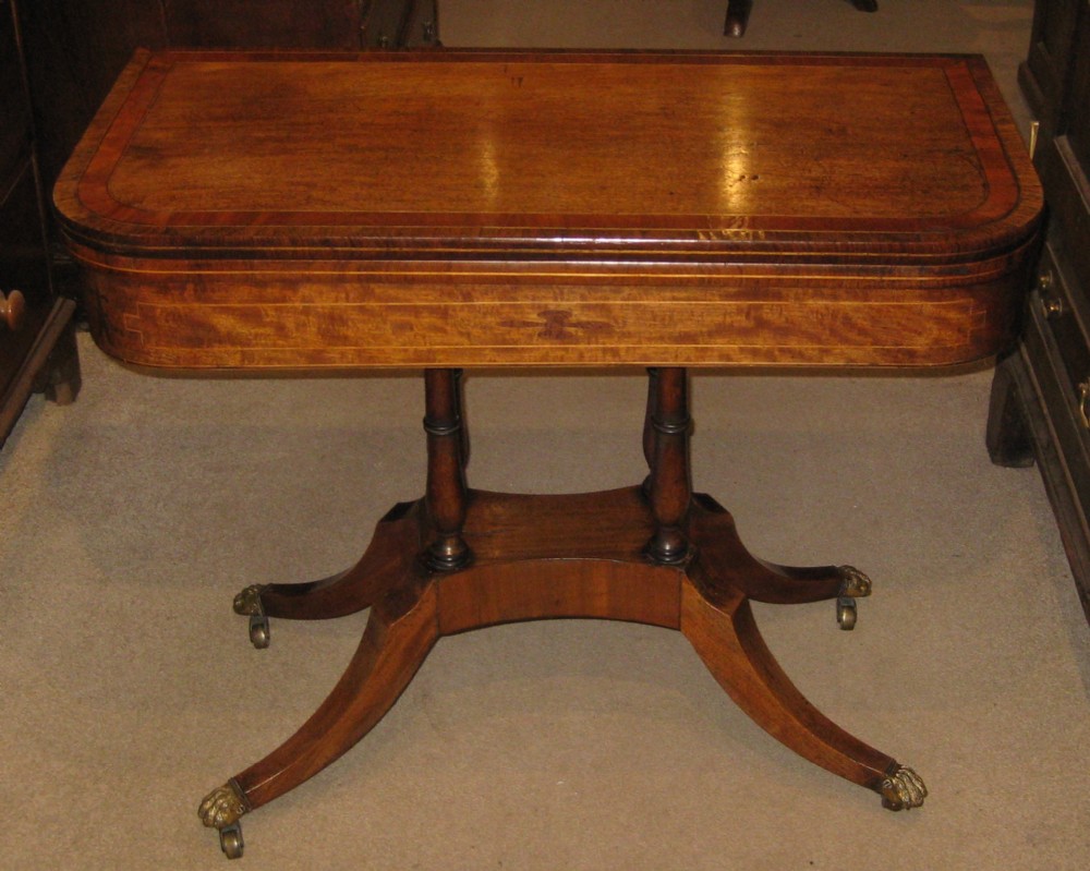 An early Victorian mahogany and rosewood fold-over card table featuring an inlaid frieze, twin turned supports, and splayed legs with brass paw feet.