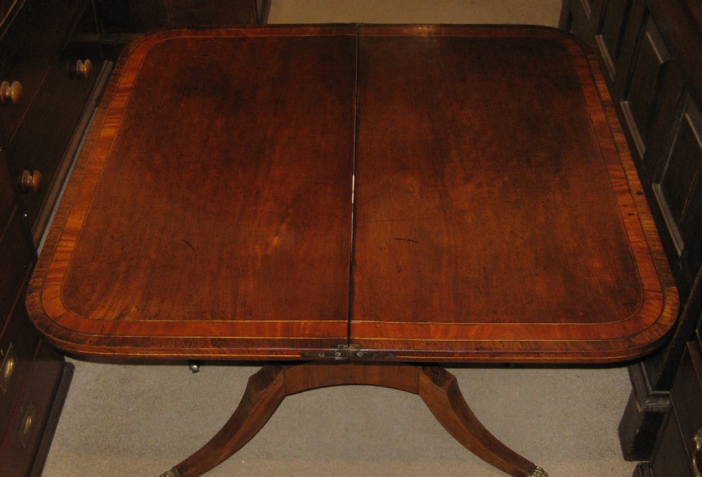 An early Victorian mahogany and rosewood fold-over card table featuring an inlaid frieze, twin turned supports, and splayed legs with brass paw feet. View III