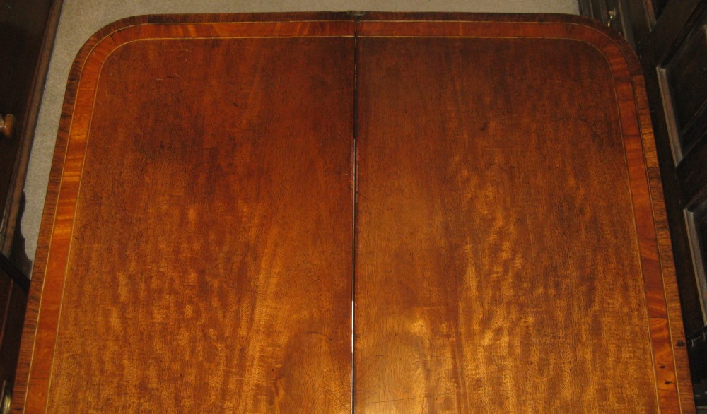 An early Victorian mahogany and rosewood fold-over card table featuring an inlaid frieze, twin turned supports, and splayed legs with brass paw feet. View VI